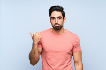Fototapeta premium Handsome young man in pink shirt over isolated blue background unhappy and pointing to the side