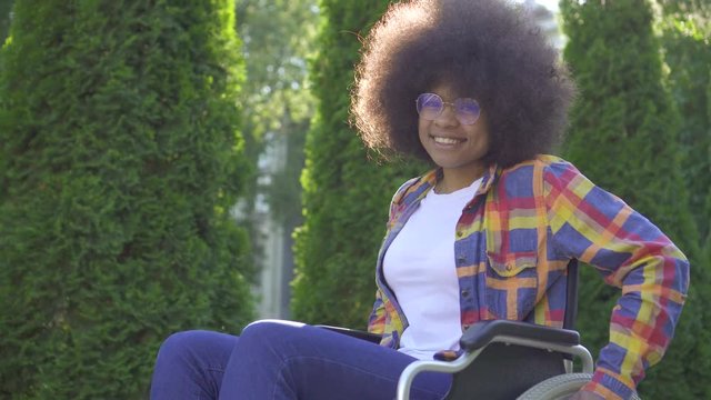 positive african woman with an afro hairstyle disabled in a wheelchair looking at the camera and smiling