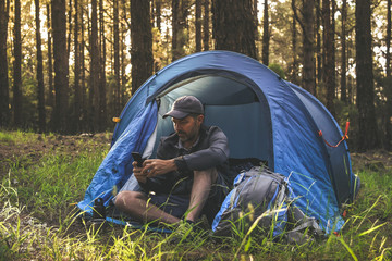 Travel blogger man making social video story in a camping tent Tourist boy communicate with smartphone in the forest with remote friend Tourism adventure active lifestyle and modern technology concept