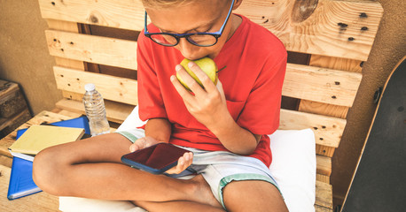 Happy trendy student taking a break and eat a fruit Healthy snack after school using smartphone...