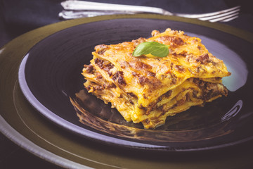 Traditional Lasagne with Minced Beef and Green Basil on Dark Plate