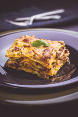 Traditional Lasagne with Minced Beef and Green Basil on Dark Plate