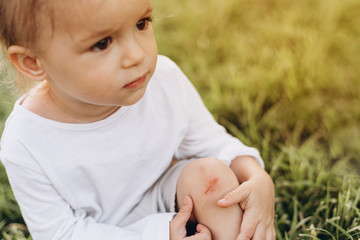 photo of a little girl who fell and scratched his knee in the blood, it hurts the wound and it...