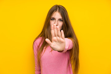 Young woman with long hair over isolated yellow wall making stop gesture