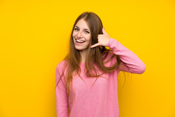 Young woman with long hair over isolated yellow wall making phone gesture. Call me back sign