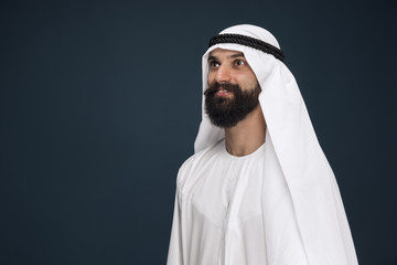 Half-length portrait of arabian saudi businessman on dark blue studio background. Young male model...