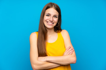 Young woman with long hair over isolated blue wall keeping the arms crossed in frontal position