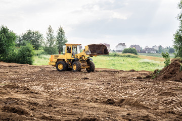 large yellow wheel loader aligns a piece of land for a new building