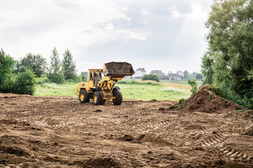 large yellow wheel loader aligns a piece of land for a new building