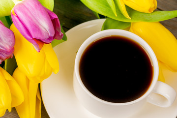 Yellow and purple tulips and coffee cup on rustic wooden table. Close up shot.