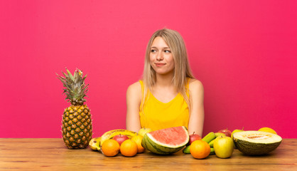 Young blonde woman with lots of fruits standing and looking to the side