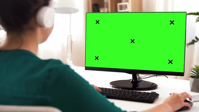 technology, post production and people concept - woman in headphones with chroma key green screen on computer at home office