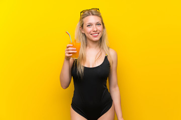 Young woman in swimsuit over yellow background with a cocktail