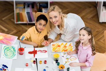 Fototapeta premium overhead view of cheerful teacher smiling with happy multicultural kids