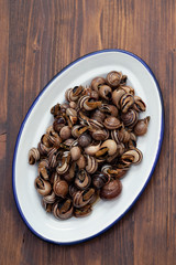 boiled snails with herbs in white dish on wooden background