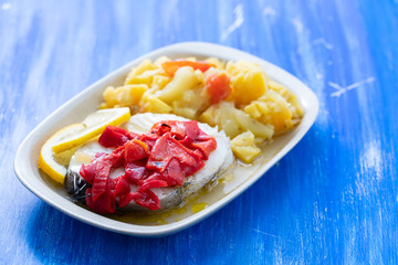 boiled fish with red pepper, vegetables and olive oil on white dish