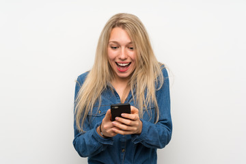 Young blonde woman over isolated white wall surprised and sending a message