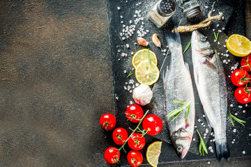Raw sea bass fish with spices and ingredients, ready for cooking, dark concrete background copy...