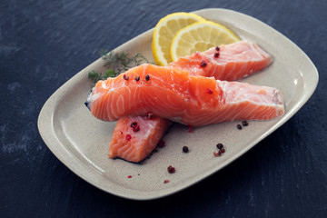 raw salmon with dill and lemon on white dish on ceramic background