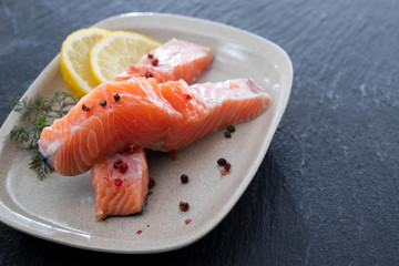 raw salmon with dill and lemon on white dish on ceramic background