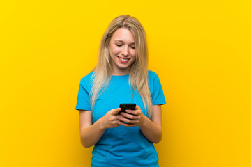 Young blonde woman over isolated yellow background sending a message with the mobile