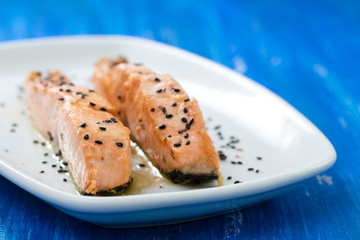 grilled salmon with black sesame on white dish on blue wooden background