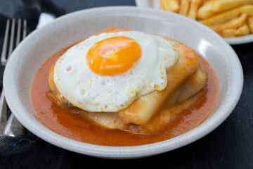 typical portuguese dish francesinha in dish on black ceramic background