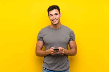 Handsome man over isolated yellow wall sending a message with the mobile