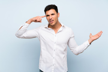 Handsome man over blue wall making the gesture of madness putting finger on the head