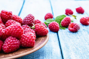 Ripe red raspberries on a bowl against the background of blue boards. Selective focus.