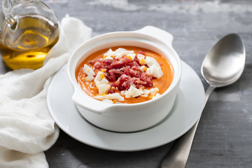 Typical Spanish soup salmorejo cream with ham and egg in white bowl on ceramic background. Top view.