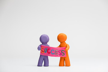 Two people made from plasticine holding a poster with the word success written on it, on white background, aligned in the center.
