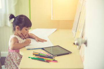 Little Asian child using a pencil to write on notebook at the desk