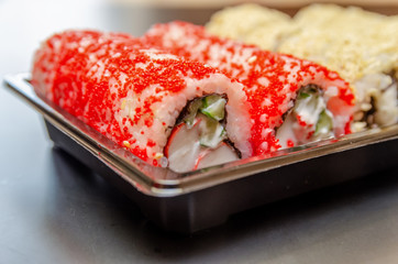 Japanese food rolls in a plastic box. A set of kunut covered sushi and red caviar in a plastic box on a black background close-up. Sushi takeaway or sushi delivery.