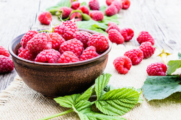 Ripe red raspberries on a bowl on the background of old boards. Selective focus.