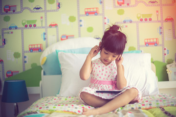 Asian children using headphone for listen music by smartphone on the bed in her decorated bedroom