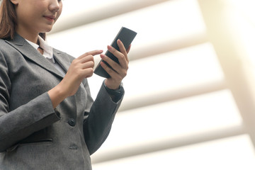 Businesswoman using smartphone in her hand while working on internet.  Young woman wearing suit while chatting digital mobile on through application at urban city.