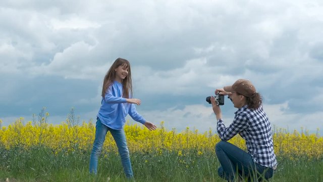 A photographer takes pictures of a funny child. A woman with a photographer takes pictures of a cheerful young girl in nature.