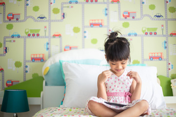 Asian children using headphone for listen music by smartphone on the bed in her decorated bedroom