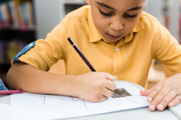 selective focus of cute african american kid drawing with pencil