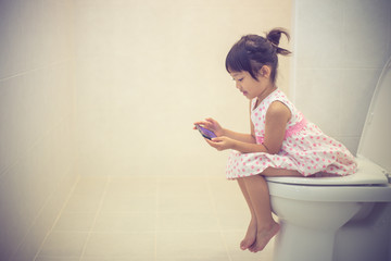 asian children sitting on a toilet and holding smartphone.
