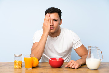 Handsome man in having breakfast covering a eye by hand
