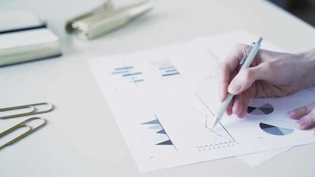 Woman fills data in graphs on paper. Records information. Woman is engaged in office work. Graphic charts,indicators. Woman works at the offside table. Woman draws symbols on the paper