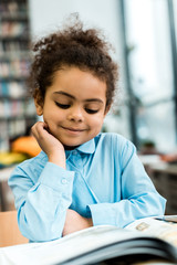 selective focus of happy african american kid smiling and looking at book on table