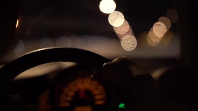 man driving car through tunnel in night time, hand on steering wheel with blurred street light bokeh