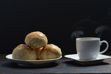 Chinese moon cake next to a steaming hot cup of coffee in front of a black background
