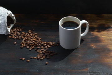 top down view of a steaming hot mug of coffee next to coffee beans in front of a black background