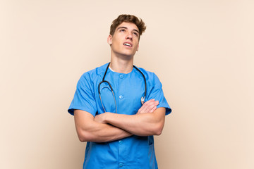 Surgeon doctor young man over isolated wall looking up while smiling