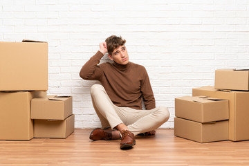 Handsome young man moving in new home among boxes having doubts and with confuse face expression