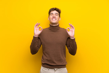 Handsome young man over isolated yellow background in zen pose